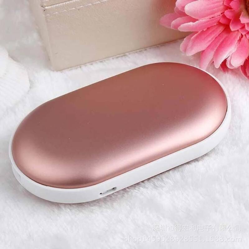 Rose gold and white handheld warmer on a soft surface with a pink flower in the background