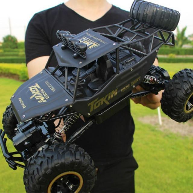 Person holding a large black and yellow RC truck with 'Tokin' branding outdoors.